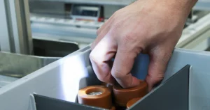 An employee removes goods from a storage compartment that is illuminated by a pick-by-light system.
