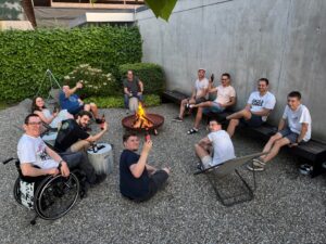 Mitarbeitende von MIA Systems sitzen am Abend gemeinsam um ein Lagerfeuer im Firmenhof, mit Getränken in der Hand und entspannter Stimmung.