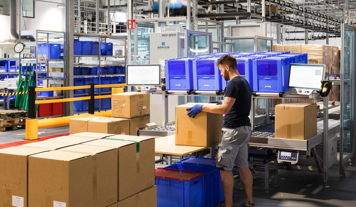 Ein Lagermitarbeiter arbeitet an einer Station mit einem Karton und nutzt digitale Prozesse zur effizienten Auftragsabwicklung.